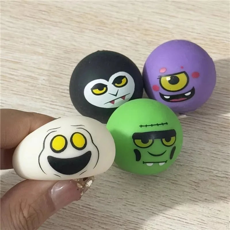 Four cartoon monster stress balls in black, purple, green, and cream, with a hand holding one cream-colored ball, set against a light wood background.