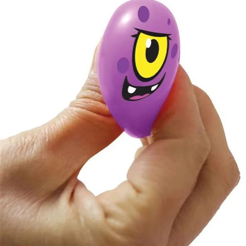 A hand holding a mini needoh squishkin shaped like a cartoon monster with a large yellow eye and black details, against a plain white background.